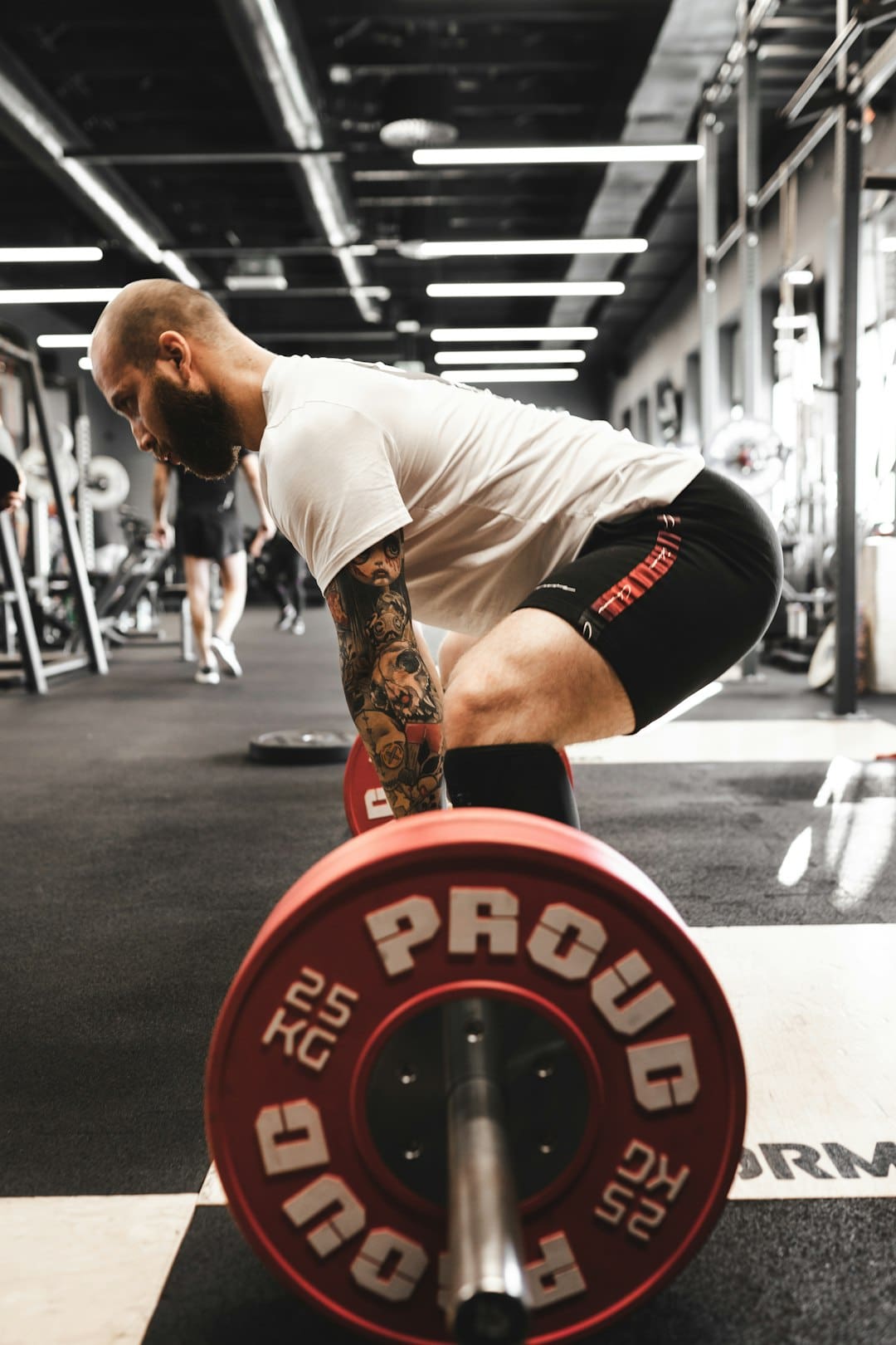 man-in-white-t-shirt-and-black-shorts-carrying-red-and-black-barbell-ui45pygusby